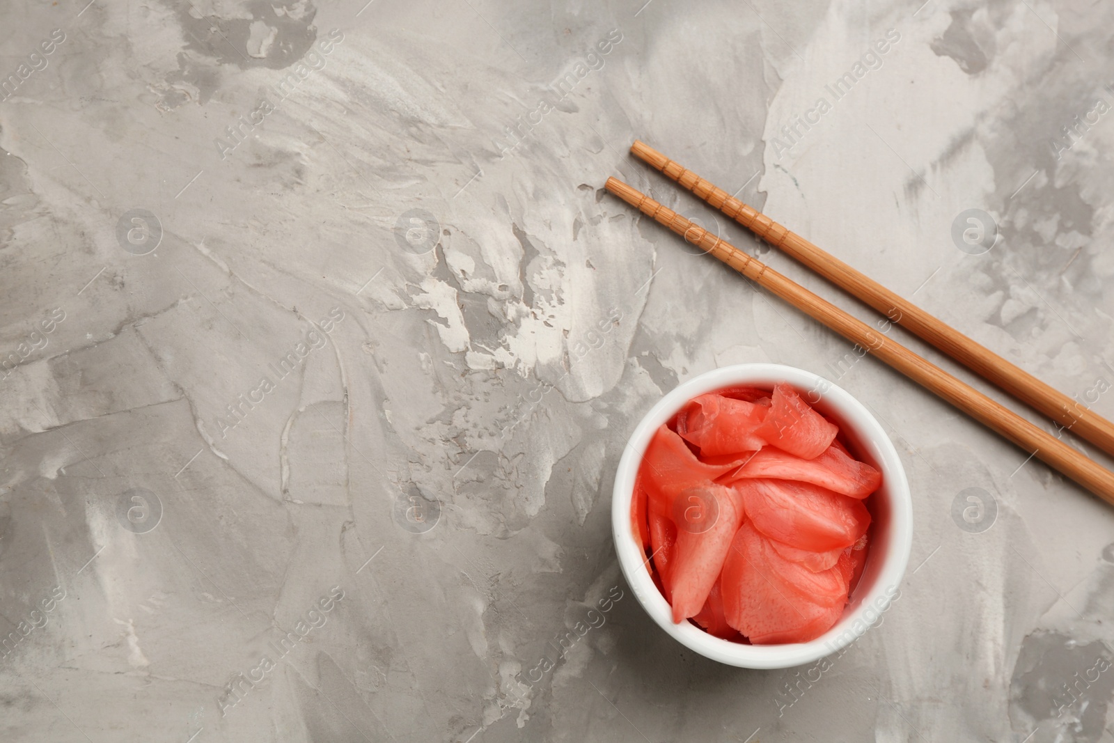 Photo of Spicy pickled ginger and chopsticks on grey table, flat lay. Space for text