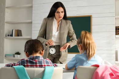 Photo of Teacher with alarm clock scolding pupils for being late in classroom