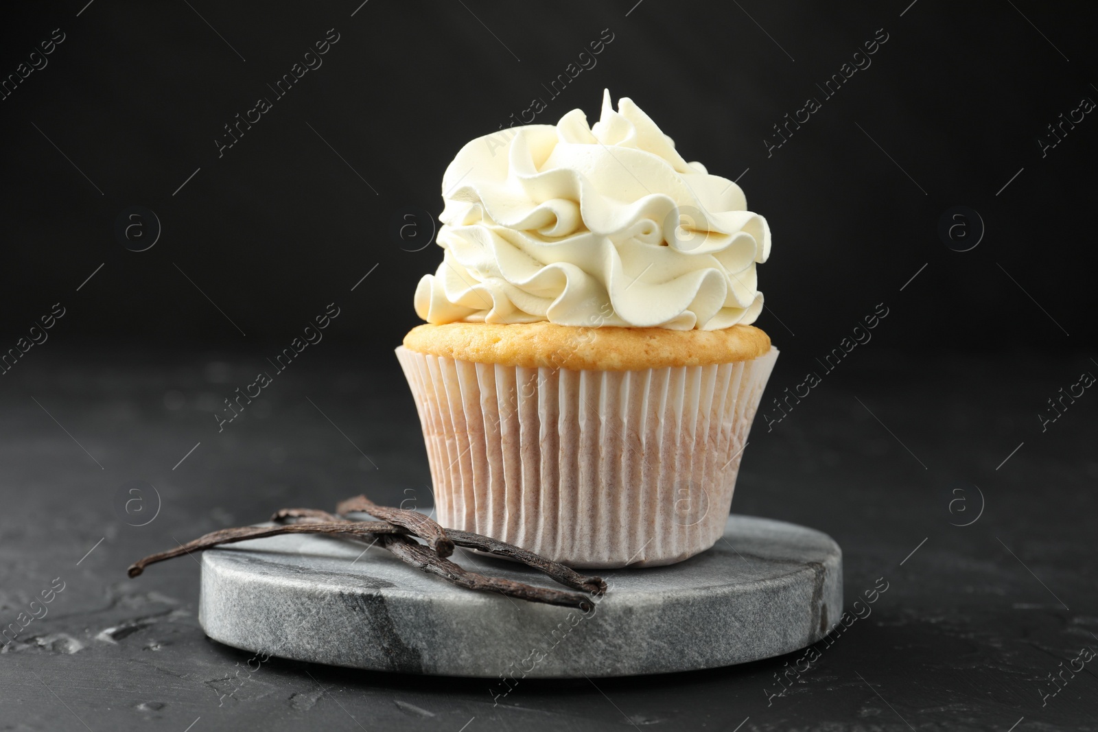 Photo of Tasty cupcake with cream and vanilla pods on black table, closeup