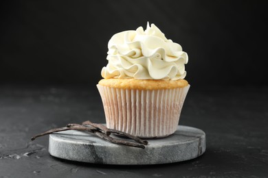 Photo of Tasty cupcake with cream and vanilla pods on black table, closeup