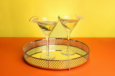 Photo of Martini glasses of refreshing cocktail with lemon slices and rosemary on orange table