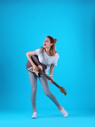 Young woman playing electric guitar on color background