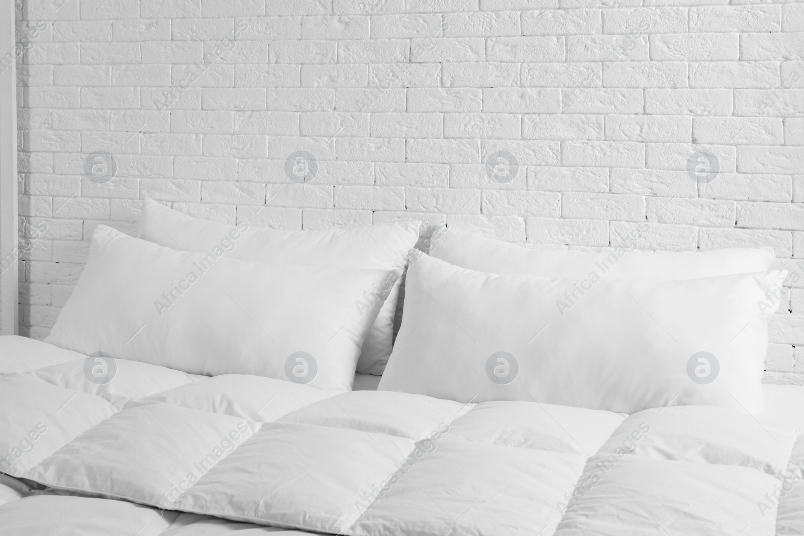 Photo of Large comfortable bed with pillows and blanket near white brick wall indoors. Stylish interior