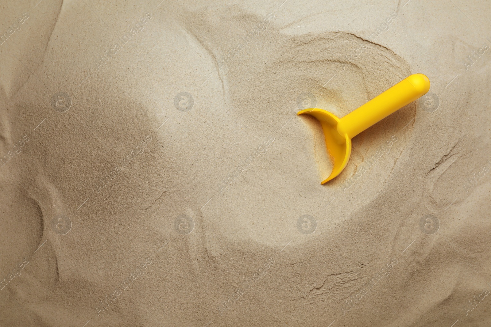 Photo of Bright plastic toy shovel on sand, top view