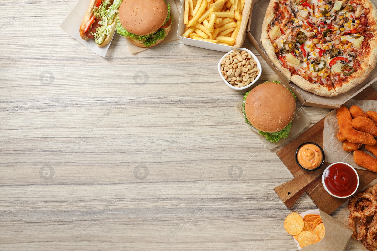 Photo of French fries, pizza and other fast food on wooden table, flat lay with space for text