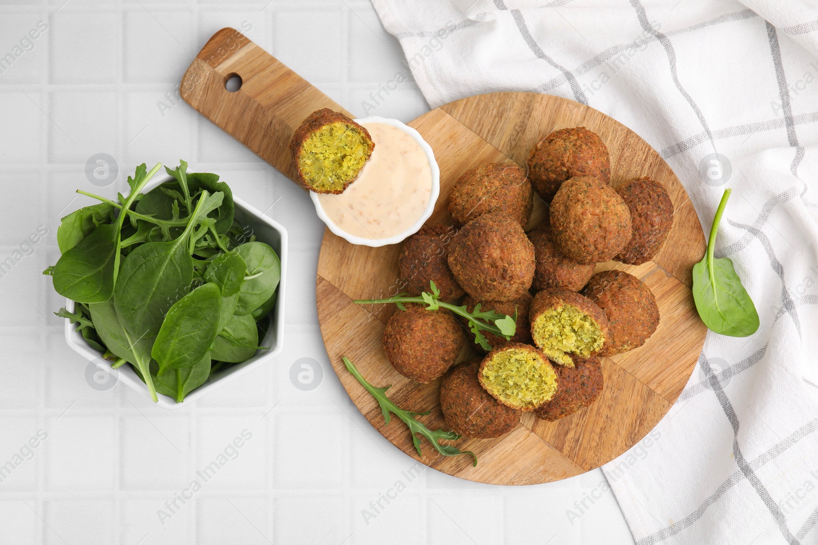 Photo of Delicious falafel balls, herbs and sauce on white tiled table, top view