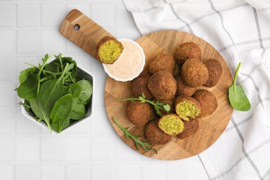 Photo of Delicious falafel balls, herbs and sauce on white tiled table, top view