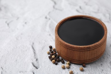 Photo of Wooden bowl with balsamic vinegar and peppercorns on white textured table, closeup. Space for text