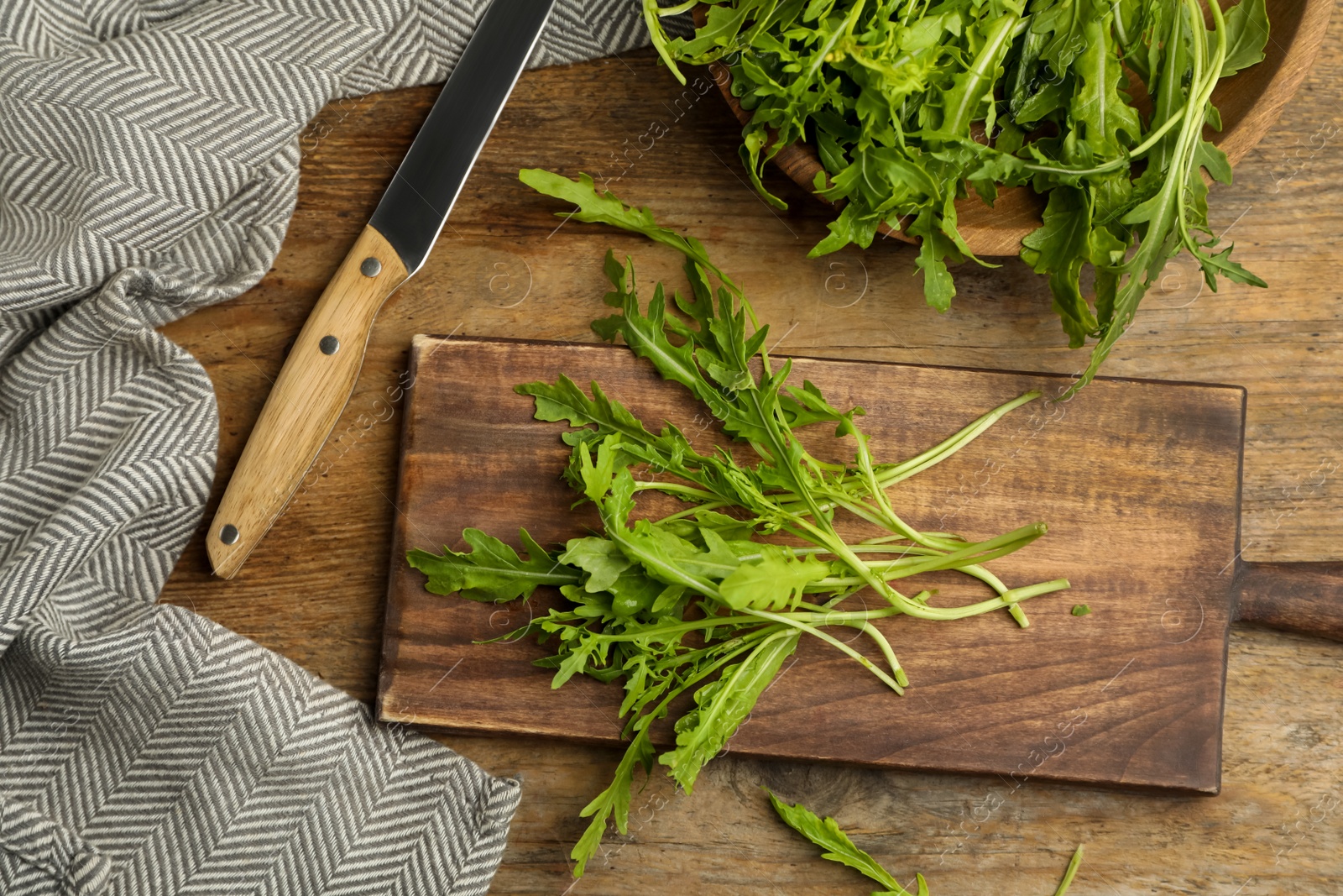 Photo of Fresh arugula, cutting board and knife on wooden table, flat lay