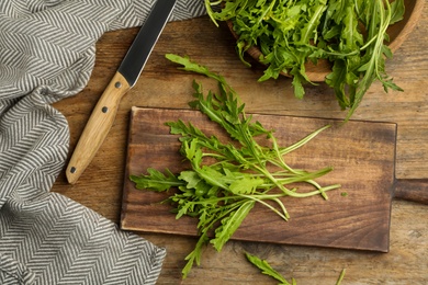 Fresh arugula, cutting board and knife on wooden table, flat lay