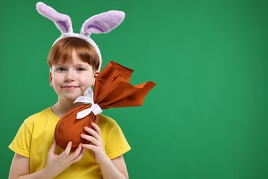 Photo of Easter celebration. Cute little boy with bunny ears and wrapped egg on green background. Space for text