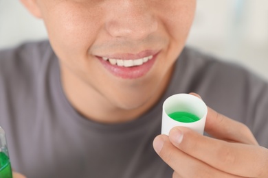 Man holding cap with mouthwash, closeup view. Teeth care