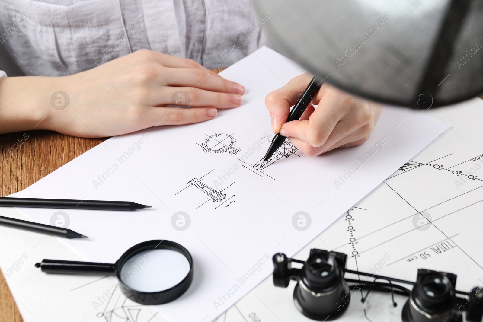 Photo of Jeweler drawing sketch of elegant ring on paper at wooden table, closeup