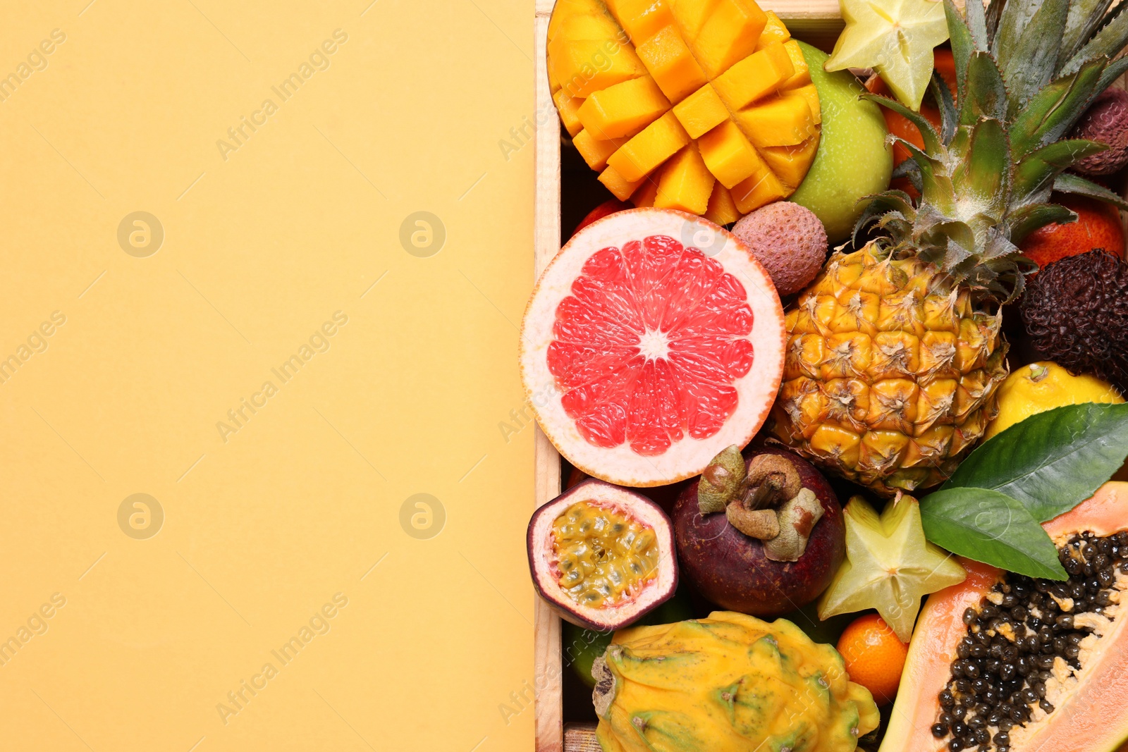 Photo of Crate with different exotic fruits on yellow background, top view. Space for text