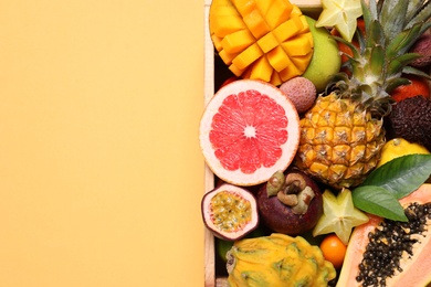Crate with different exotic fruits on yellow background, top view. Space for text