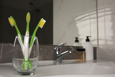 Photo of Glass holder with light green toothbrushes in bathroom