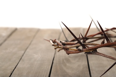 Photo of Crown of thorns on wooden table against white background, closeup with space for text. Easter attribute