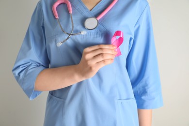 Photo of Mammologist with pink ribbon on light background, closeup. Breast cancer awareness