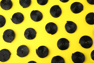 Tasty black liquorice candies on yellow background, flat lay