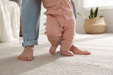Photo of Mother supporting her baby daughter while she learning to walk at home, closeup