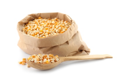 Photo of Paper bag and spoon with raw corn kernels on white background. Healthy grains and cereals