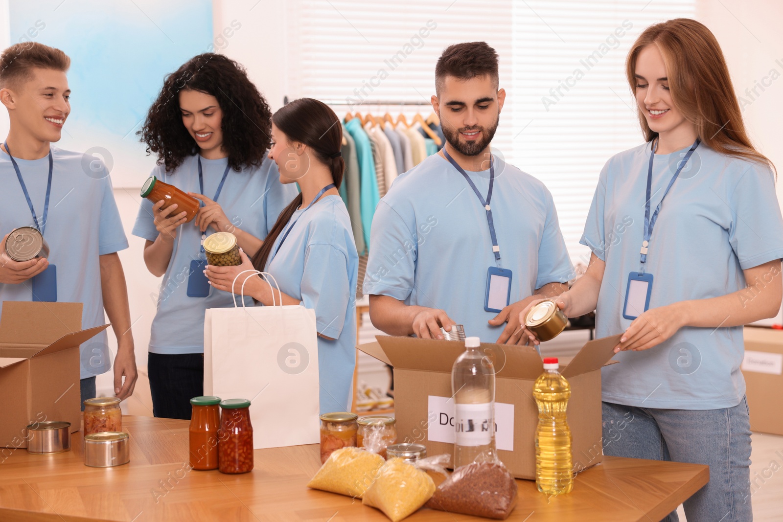 Photo of Group of volunteers packing food products at table indoors