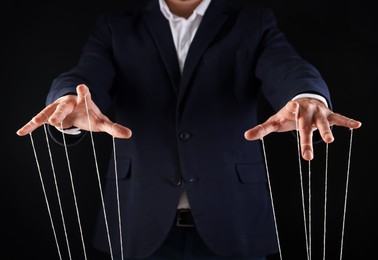 Photo of Man in suit pulling strings of puppet on black background, closeup