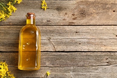 Photo of Rapeseed oil in glass bottle and beautiful yellow flowers on wooden table, flat lay. Space for text