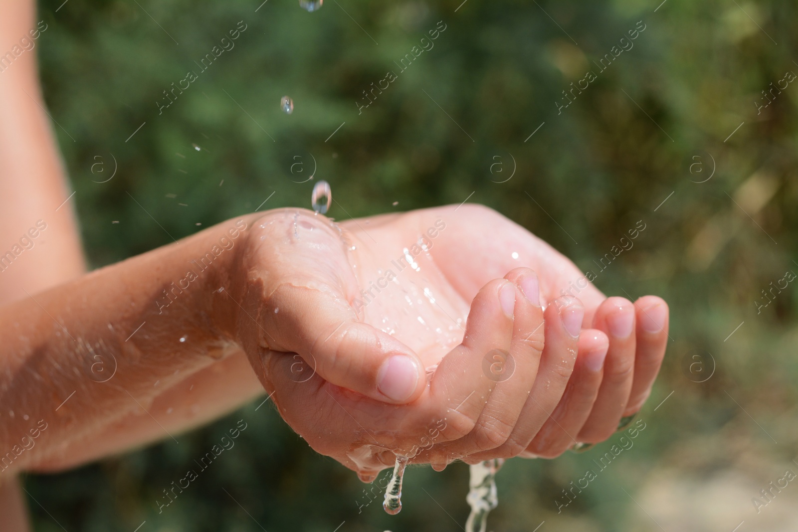 Photo of Pouring water into kid`s hands outdoors, closeup