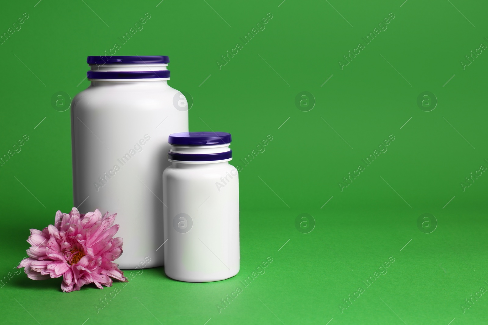 Photo of Plastic medicine bottles and pink flower on green background, space for text. Medicament