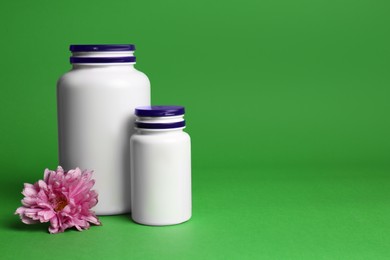 Plastic medicine bottles and pink flower on green background, space for text. Medicament