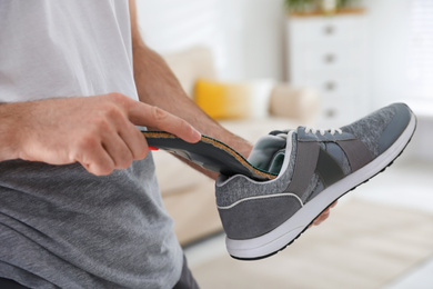 Man putting orthopedic insole into shoe at home, closeup