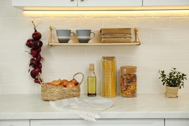 Photo of Fresh onions and other products on white countertop in modern kitchen