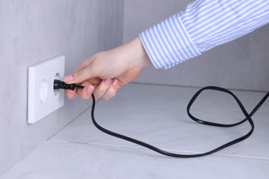 Woman inserting electric plug into socket at white table indoors, closeup