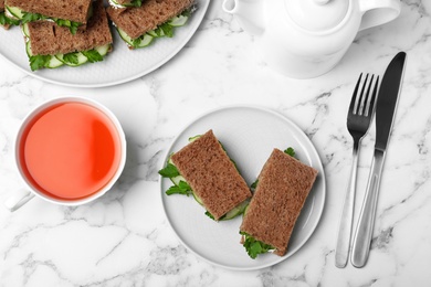 Photo of Flat lay composition with traditional English cucumber sandwiches and tea set on marble background