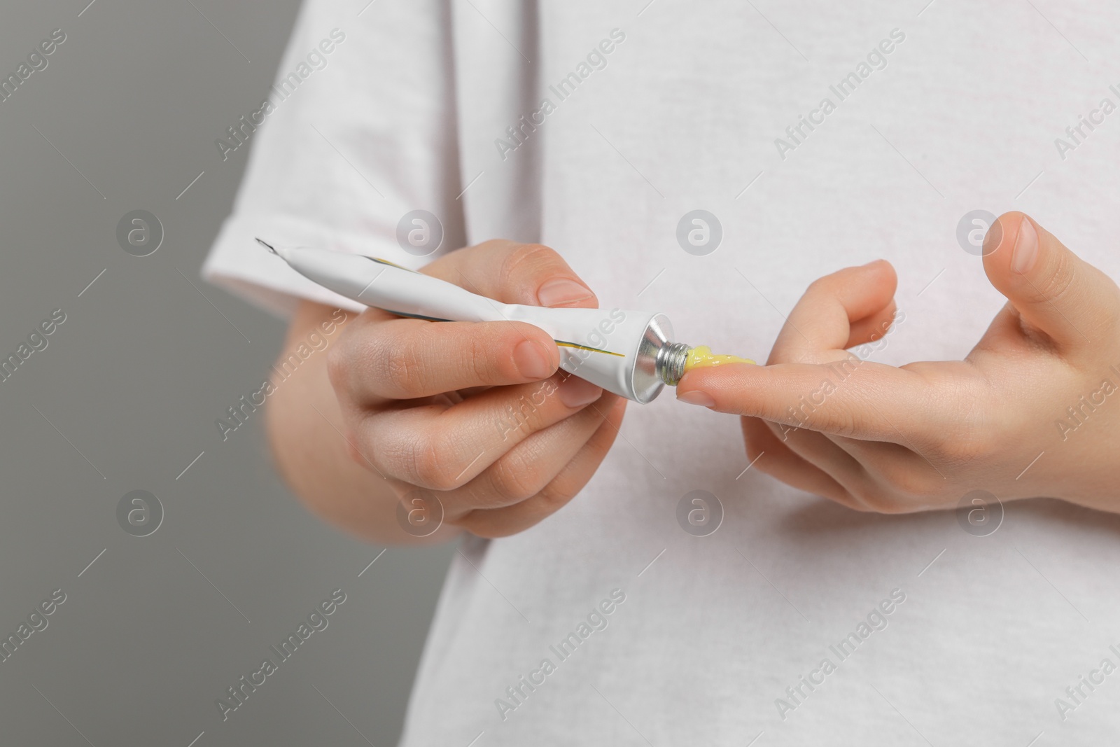 Photo of Child applying ointment onto hand against grey background, closeup