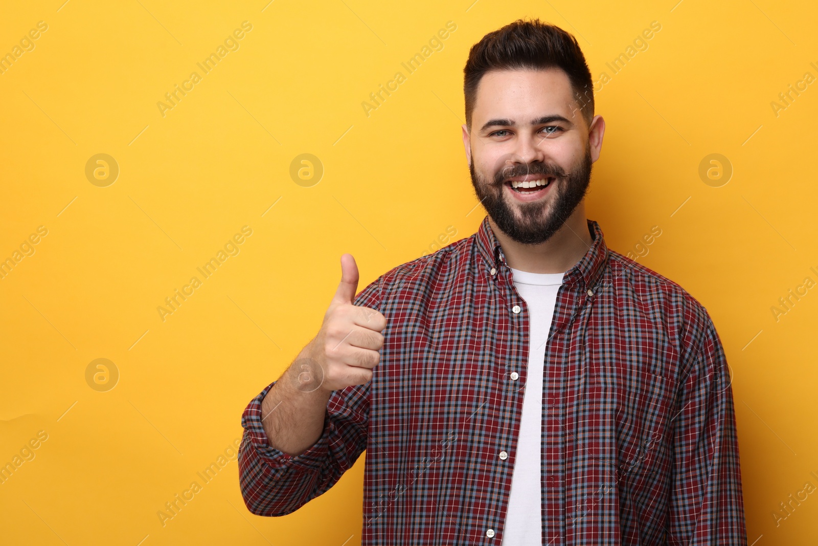Photo of Happy young man with mustache showing thumb up on yellow background. Space for text
