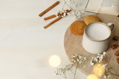 Photo of Cup of hot beverage, cookies, brown sugar and flowers on white wooden table, bokeh effect. Space for text