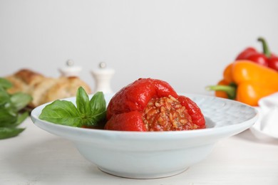 Delicious stuffed pepper with basil in bowl on white table, space for text