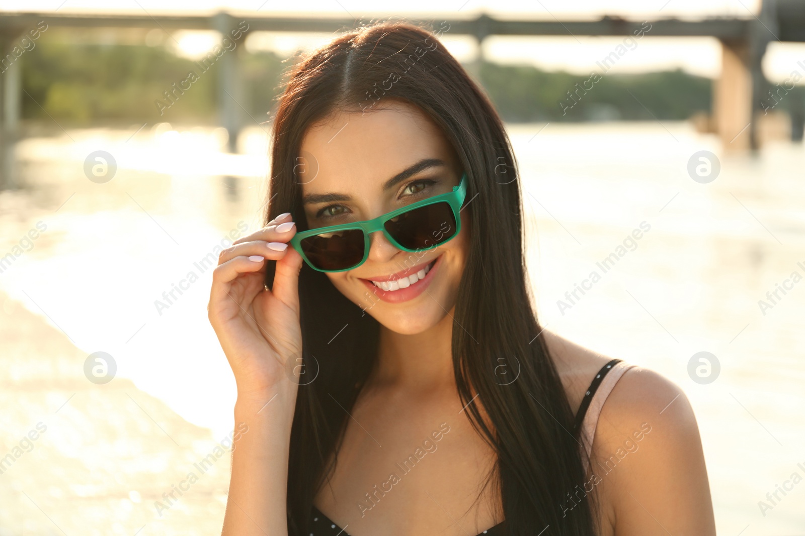 Photo of Beautiful young woman wearing stylish sunglasses near river