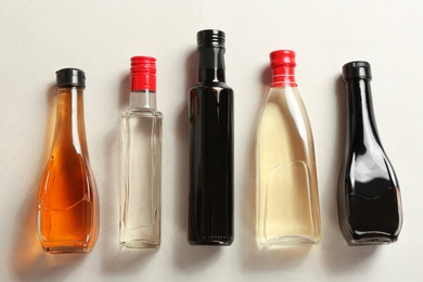 Photo of Bottles with different kinds of vinegar on light table, top view