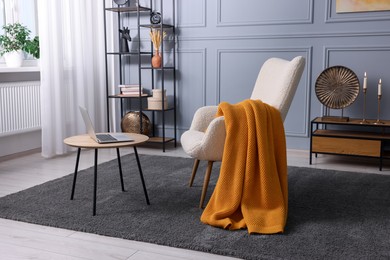 Photo of Living room interior with comfortable armchair, blanket and side table