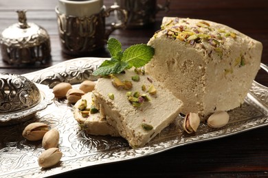 Photo of Tasty halva with pistachios and mint on wooden table, closeup