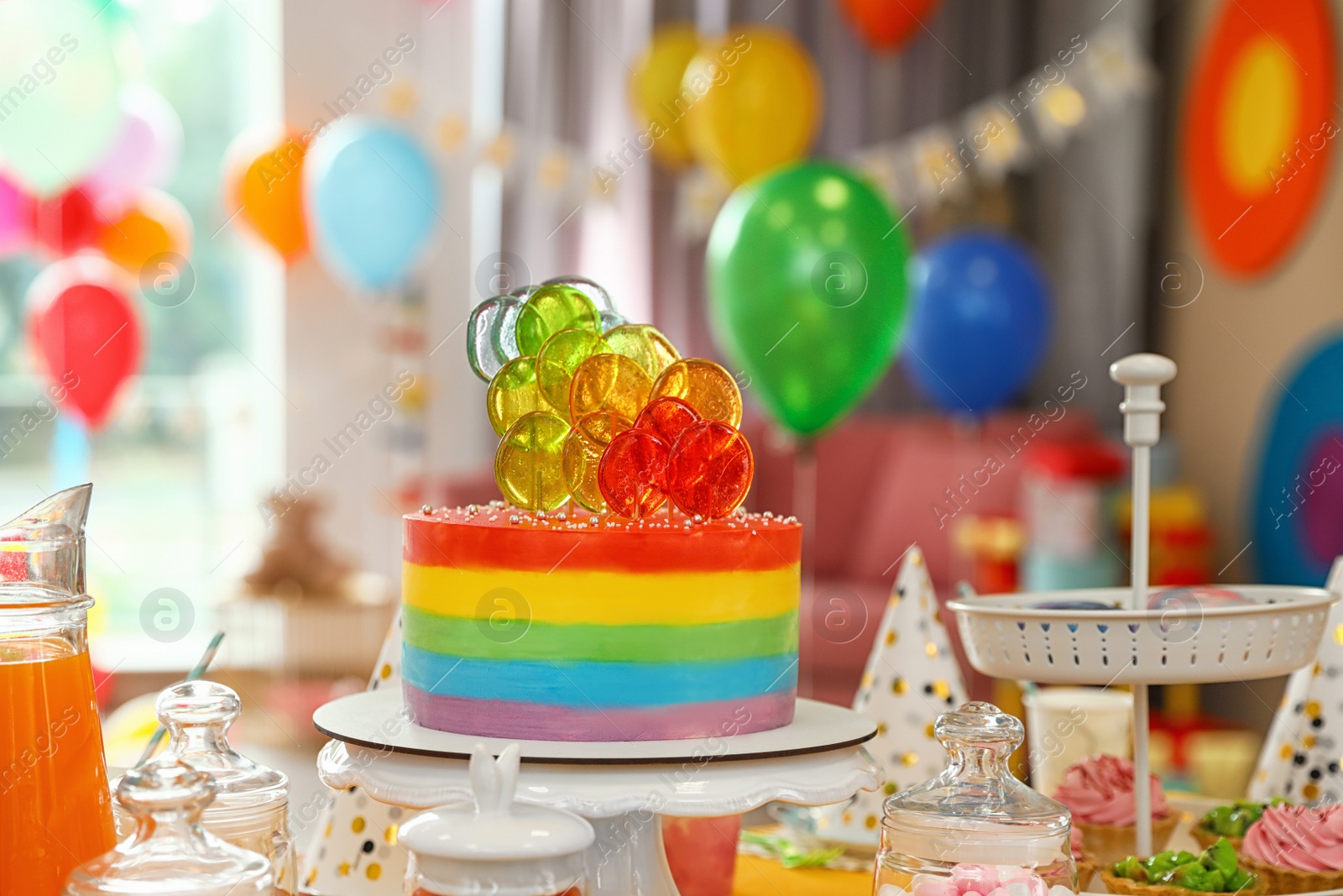 Photo of Bright birthday cake and other treats on table in decorated room