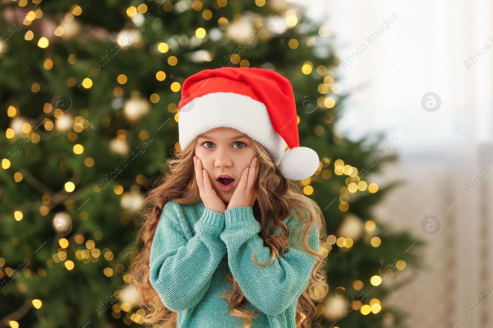 Photo of Emotional little girl near Christmas tree at home