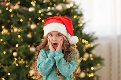 Emotional little girl near Christmas tree at home