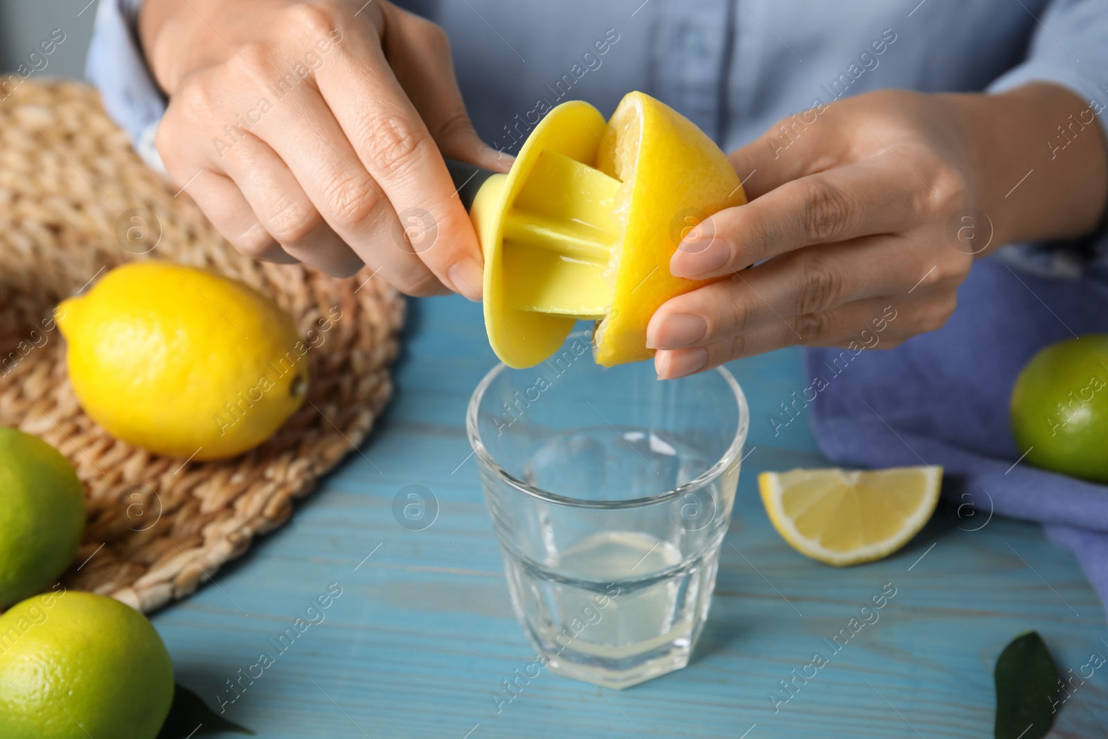 Photo of Woman squeezing lemon juice with citrus reamer at light blue wooden table, closeup