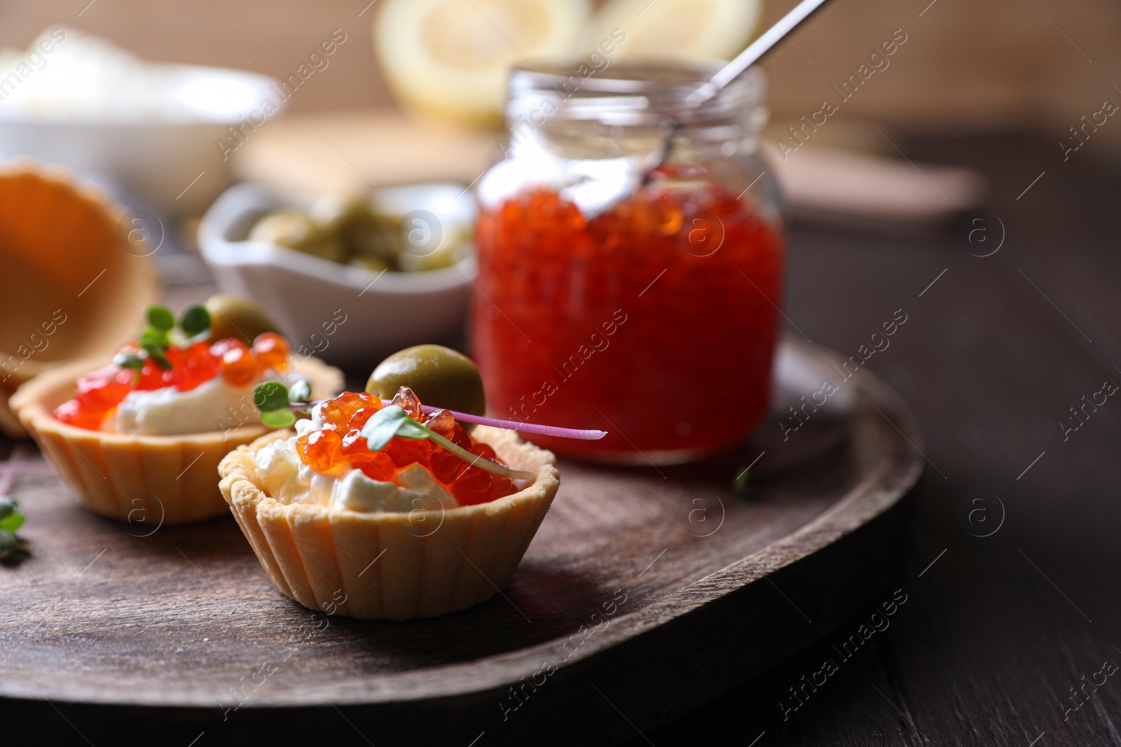 Photo of Delicious tartlets with red caviar and cream cheese served on wooden table, closeup