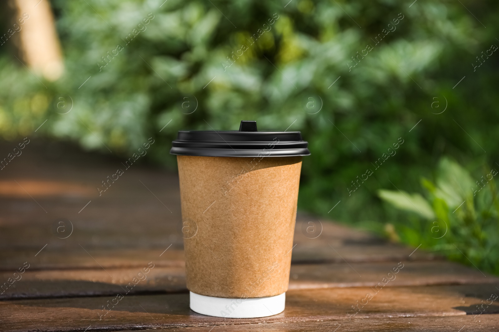 Photo of Paper cup on wooden surface outdoors. Takeaway drink