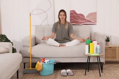 Photo of Young mother meditating on sofa in messy living room
